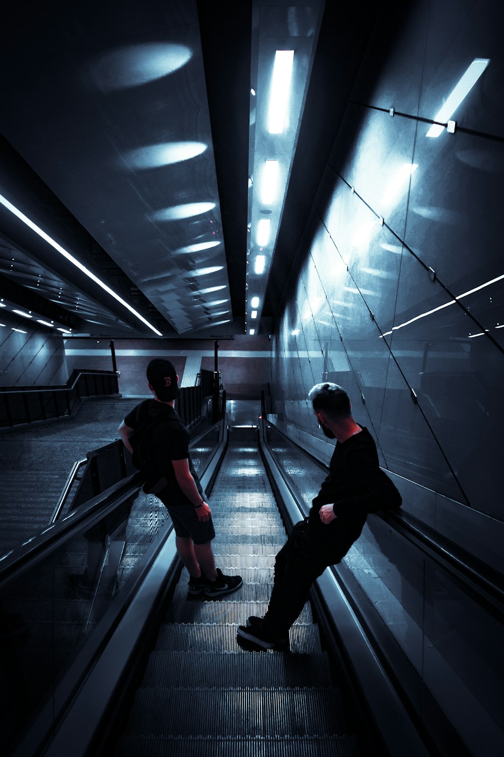 two man standing on escalator in mall