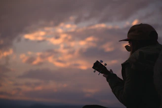 Close-up of Ebenru playing guitar with a serene sunset in the background.