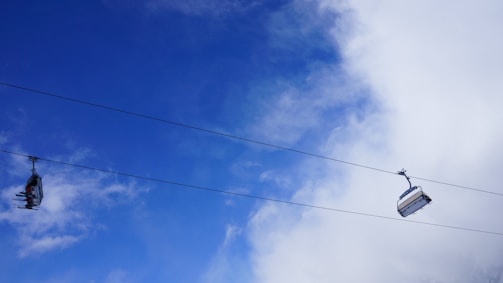 Cable cars suspended on cables traverse against a vibrant blue sky with scattered clouds, creating an open and airy atmosphere.