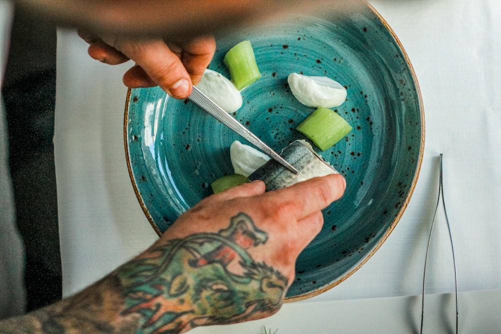 person with tattooed hand slicing fish on blue plate