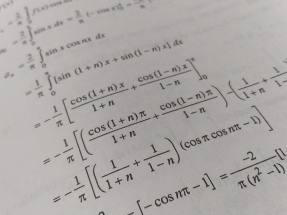 A page filled with mathematical formulas and integrals, featuring symbols and trigonometric functions such as cos and sin. The text is printed in black on an off-white background, with a slight angle giving a dynamic effect to the layout.