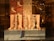 Several pairs of high-heeled boots with glossy finishes and colorful floral embroidery are displayed in a storefront. The background features decorative wallpaper with artistic bird designs. The reflection of a mannequin and interior lighting adds depth to the scene.