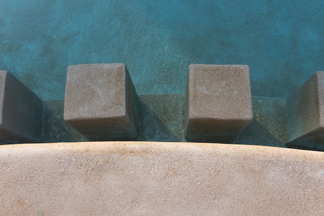 Concrete blocks protrude from a textured surface, surrounded by a smooth, curved edge. The scene appears to be part of an outdoor setting, possibly an architectural or landscape feature.