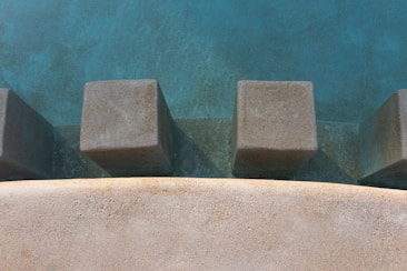 Concrete blocks protrude from a textured surface, surrounded by a smooth, curved edge. The scene appears to be part of an outdoor setting, possibly an architectural or landscape feature.