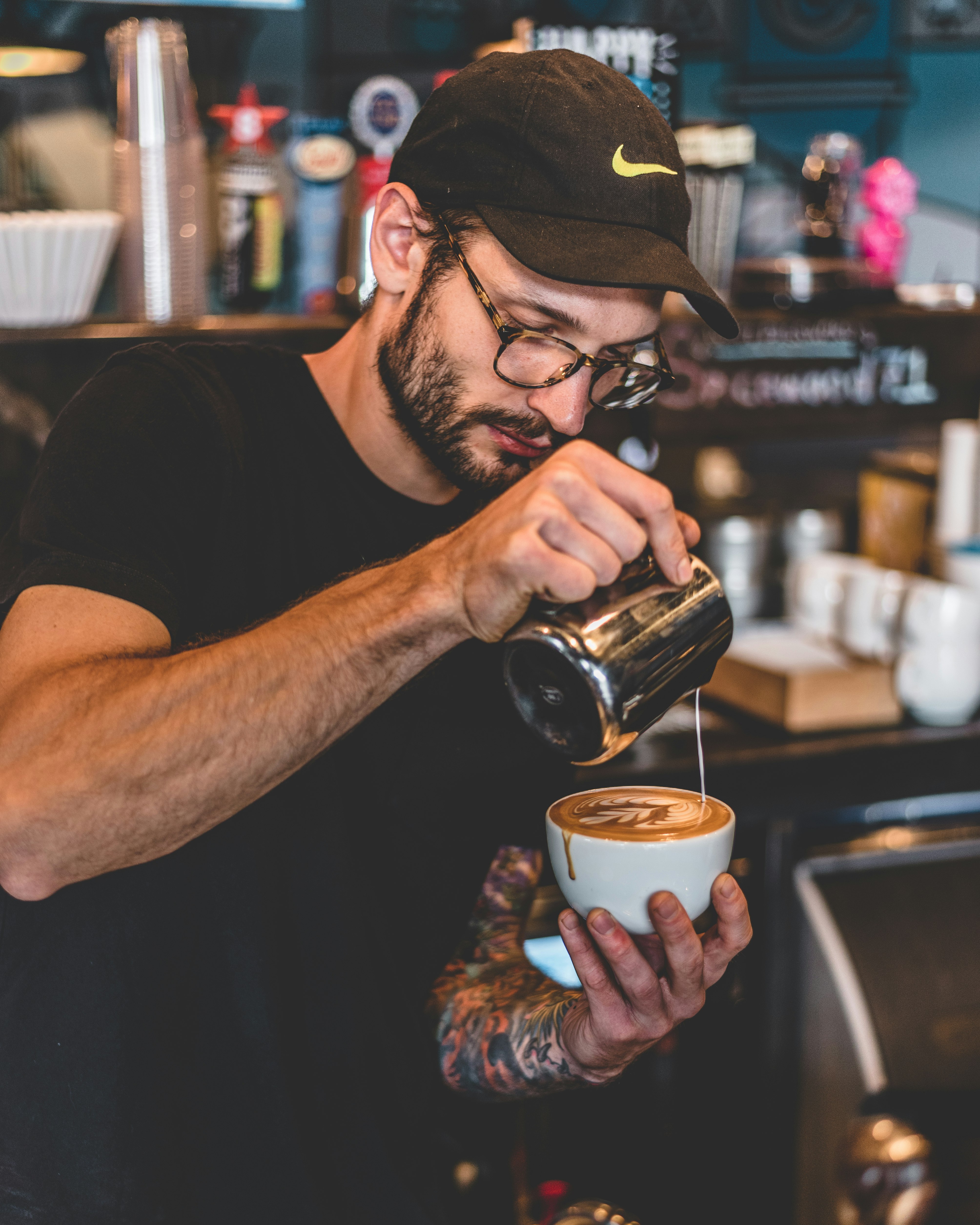 man in black shirt pouring milk on latte