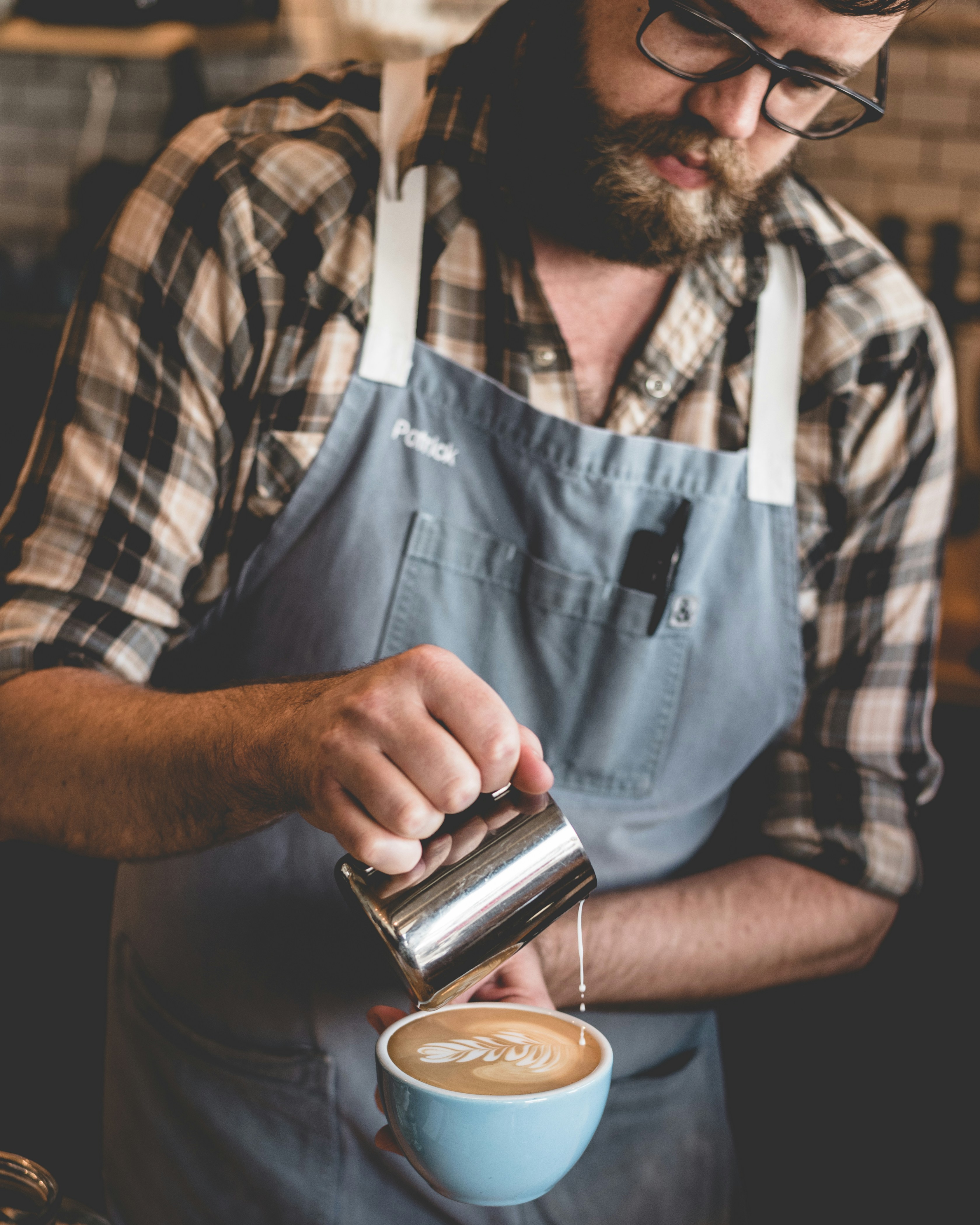 Close-up of a barista's hands pouring steamed milk into a ceramic espresso cup creating latte art