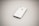 A white smartphone, identified as an Apple iPhone, is placed on a plain, light-colored surface. The phone is oriented with its back facing upwards, featuring the iconic Apple logo in the center. The image is slightly out of focus, providing a soft and minimalistic appearance.