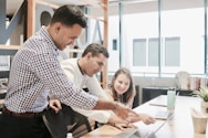 A diverse team of professionals collaborating around a laptop in a modern office setting.