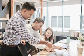 A diverse team collaborating enthusiastically around a laptop in a bright office.