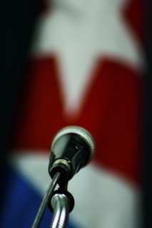 A close-up view of a microphone in the foreground with a blurry background displaying a red, white, and blue pattern and a star shape.