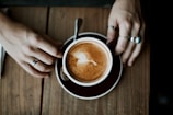 Hands adorned with delicate rings holding a cup of coffee in a cozy café.