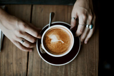 Close-up of hands adorned with minimalist rings holding a coffee cup in a cozy café setting.