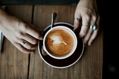 Hands adorned with delicate rings holding a cup of coffee in a cozy café.