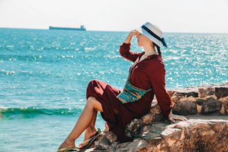 woman sitting on rock and putting right hand on her head viewing calm sea