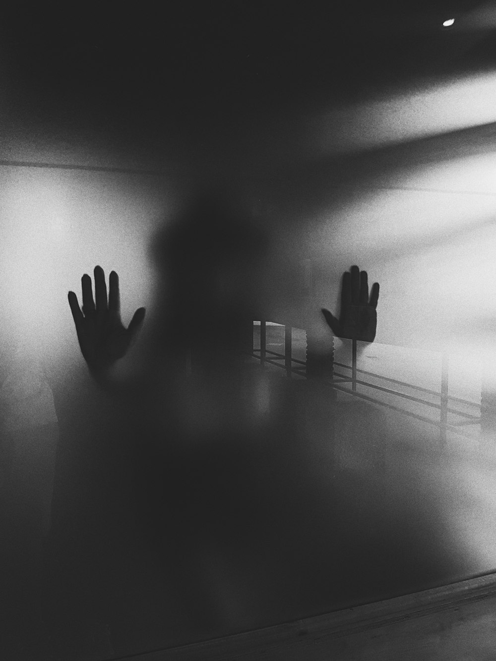 grayscale photography of person standing beside glass panel