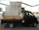 A black truck parked in an industrial area is loaded with large metal cabinets and a roll of white material. The truck's bed is wooden and surrounded by various parked vehicles in a warehouse environment.