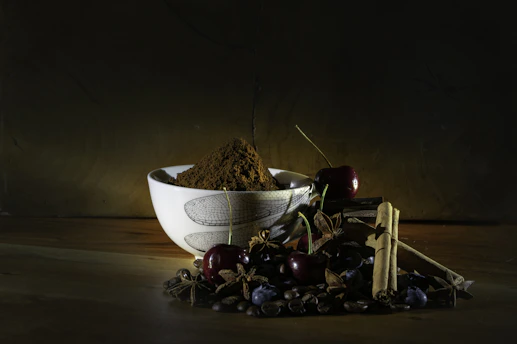 A close-up of a rustic terracotta bowl filled with vibrant Bengali spices, resting on a cream linen cloth.