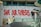 A vibrant graffiti mural with large red letters spells out 'Save Our Forests' on a white wall. The text is adorned with dripping paint, adding to the street art style. To the right, an image of a gorilla holding a spray can is partially visible. A modern walkway with a glass railing is below the mural, where two people are walking. The architecture is sleek and contemporary, featuring clean lines and a blend of glass and concrete.
