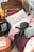 A cozy bed setup features a decorative pillow with the word 'love' embroidered on it, surrounded by various pillows and plush blankets. A dark plush octopus toy rests against the cushions. The bed is under a fabric canopy adorned with hanging star decorations. An old, distressed nightstand sits beside the bed holding a small, warmly lit lamp and some books.