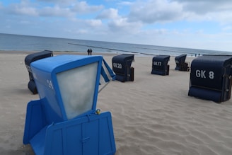 Several beach chairs with numbers are placed on a sandy beach with the ocean in the background. The sky is partly cloudy, and the scene conveys a tranquil seaside ambiance.