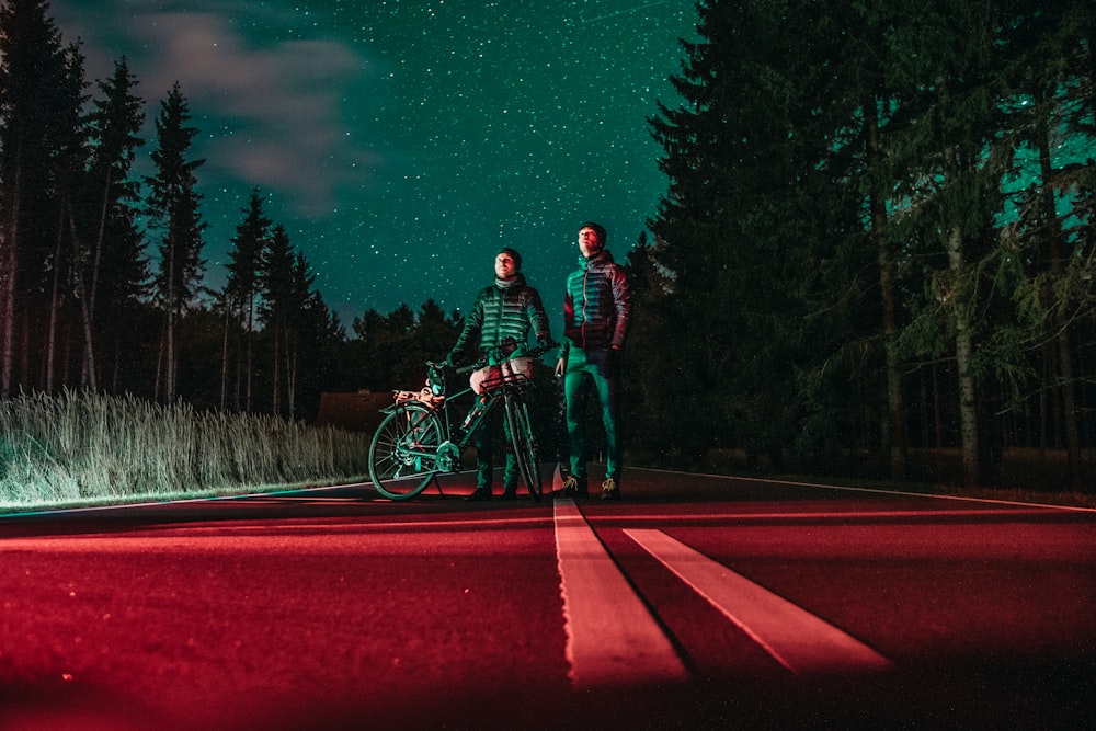 two men standing at center of road beside bicycle