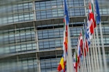 A row of various national flags on tall poles in front of a modern glass building.