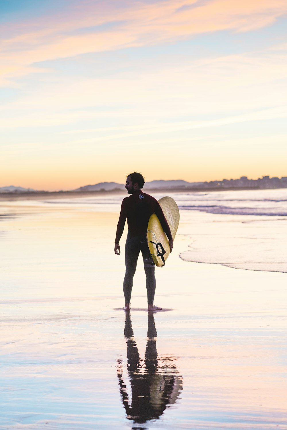 uomo che tiene la tavola da surf in piedi sulla riva