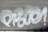 White graffiti text is spray-painted across a metallic gray roller shutter. The letters are bold and stylized, with prominent curves and loops.