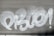 White graffiti text is spray-painted across a metallic gray roller shutter. The letters are bold and stylized, with prominent curves and loops.