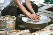 Hands gently shaping a lump of clay on a spinning wheel, surrounded by bright tools.