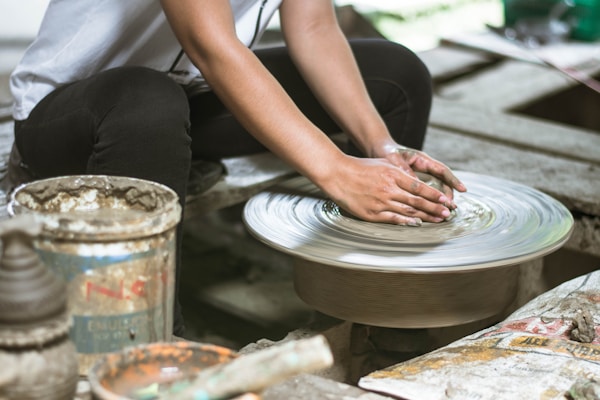 A cozy workshop scene with hands shaping clay on a pottery wheel surrounded by art supplies.