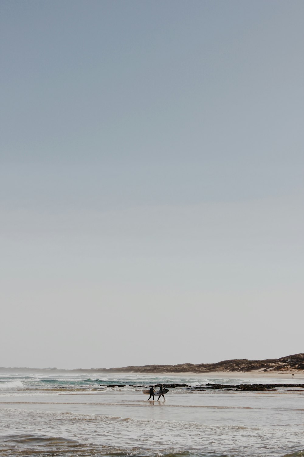 two person holding surfboards walking on seashore