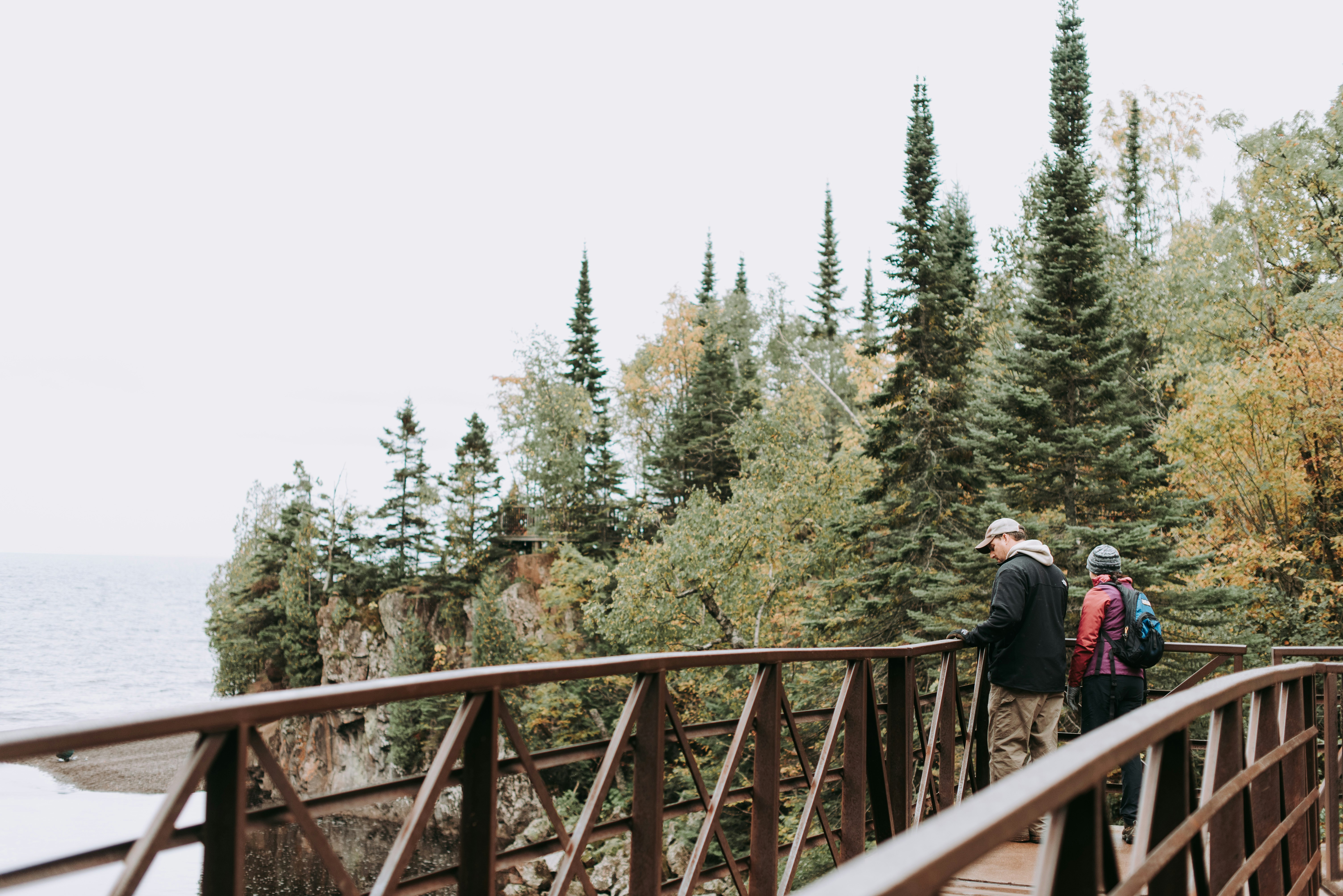 man and woman standing on wooden bridge under white clouds