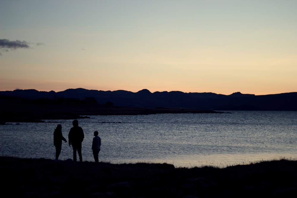 three silhouette of person standing beside body of water