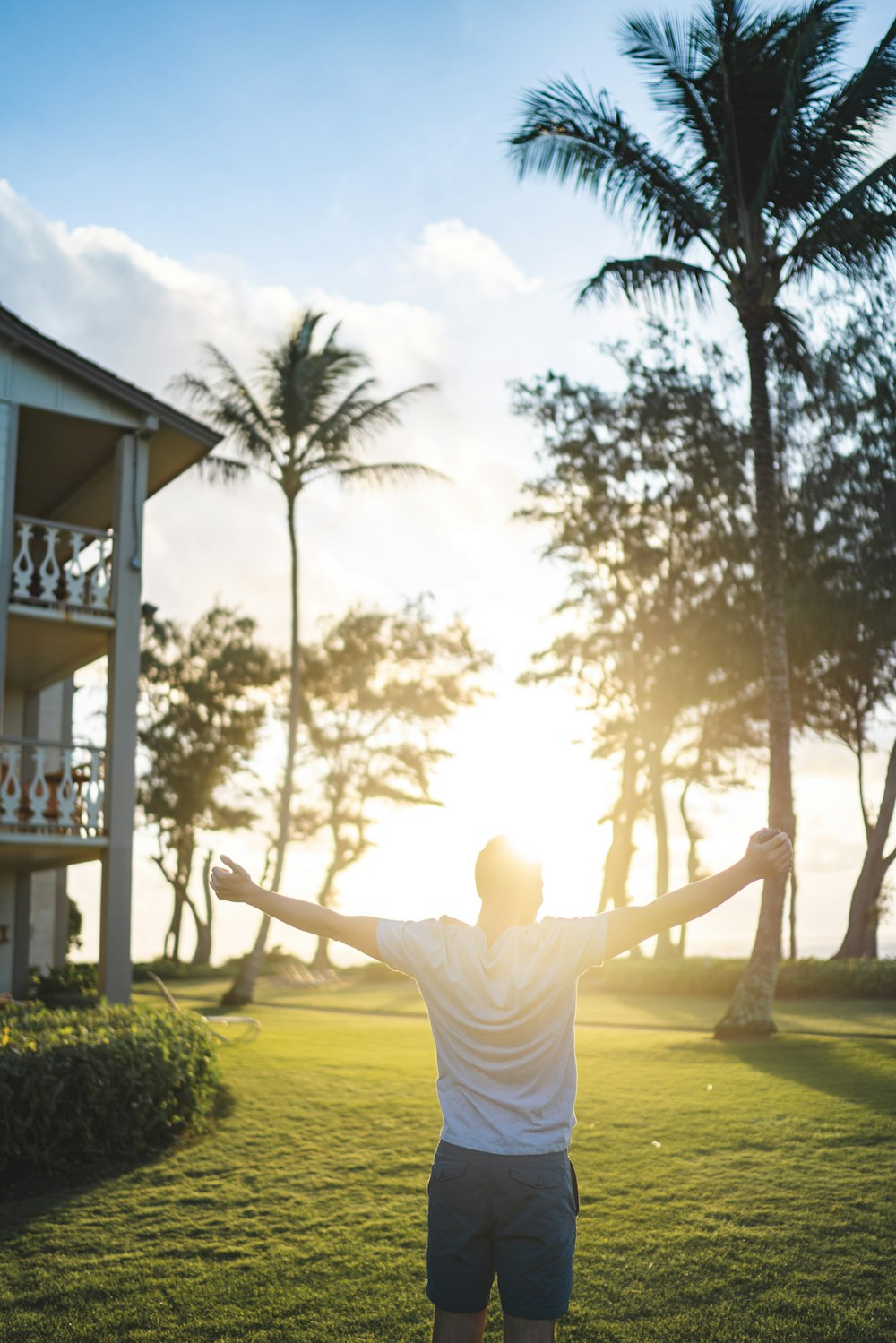 man in white shirt standing while raising hands near house