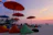 Guests relaxing under beach umbrellas while a live band plays in the background at sunset.