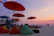 Guests relaxing under beach umbrellas while a live band plays in the background at sunset.