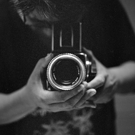 Black and white close-up of hands holding a vintage camera, emphasizing texture and light.