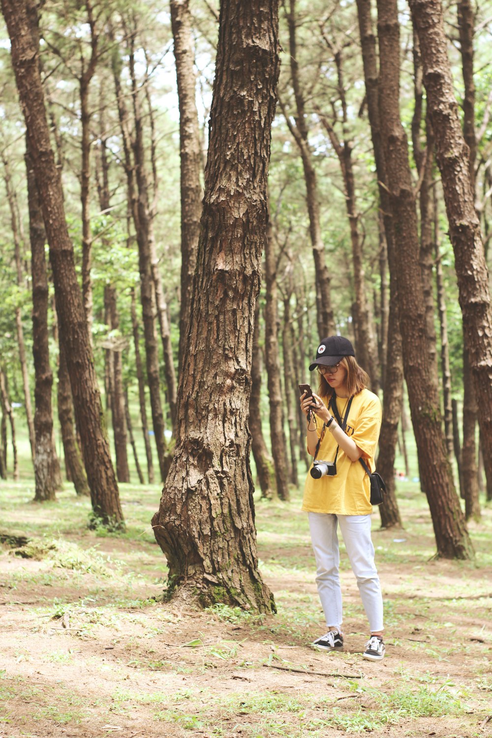 Frau steht tagsüber mit Smartphone neben Baum