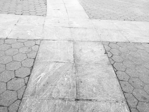 A close-up view of a paved surface featuring two different tile patterns intersecting. The left and right sides are comprised of hexagonal tiles, while the center section consists of rectangular concrete slabs. The entire surface appears weathered and is devoid of any objects or people.