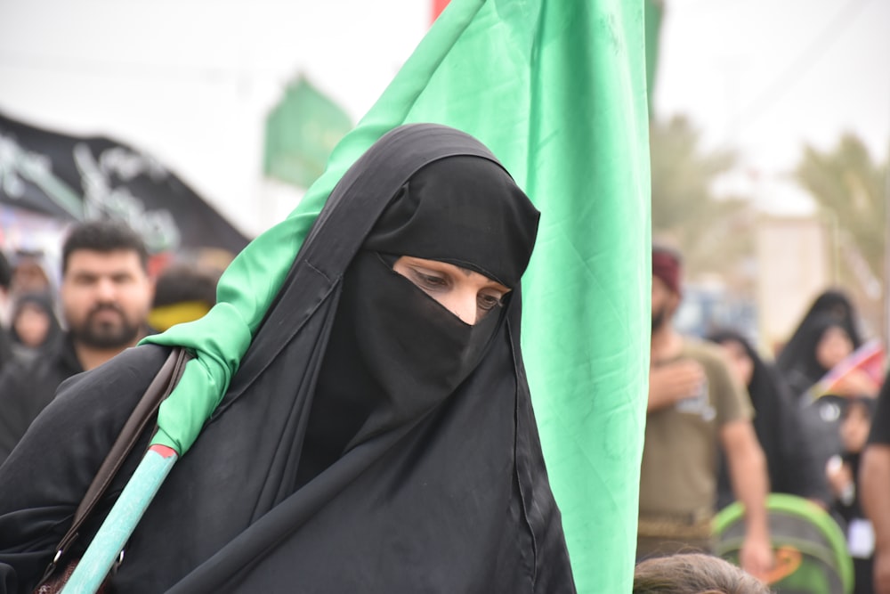 person in black hijab carrying green flag