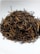 A pile of dried tea leaves featuring long, curly strands is placed on a white surface, exhibiting a mix of dark and golden hues.