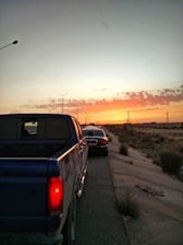 A tow truck helping a stranded SUV on a Nevada desert roadside as the sun sets.