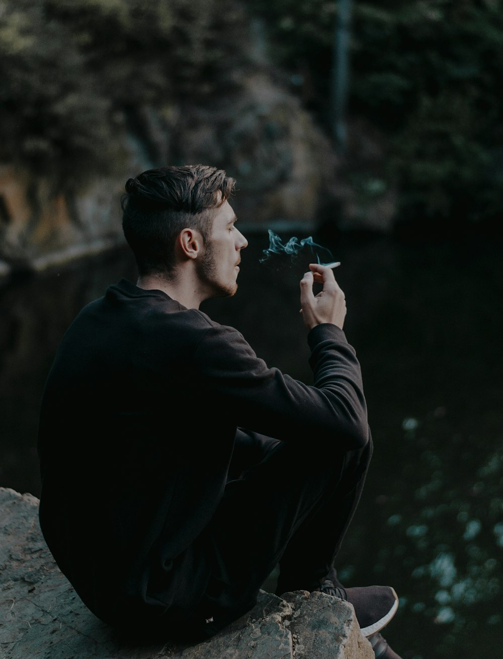 uomo che si siede sulla scogliera mentre fuma