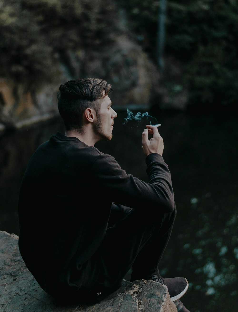 man sitting on cliff while smoking