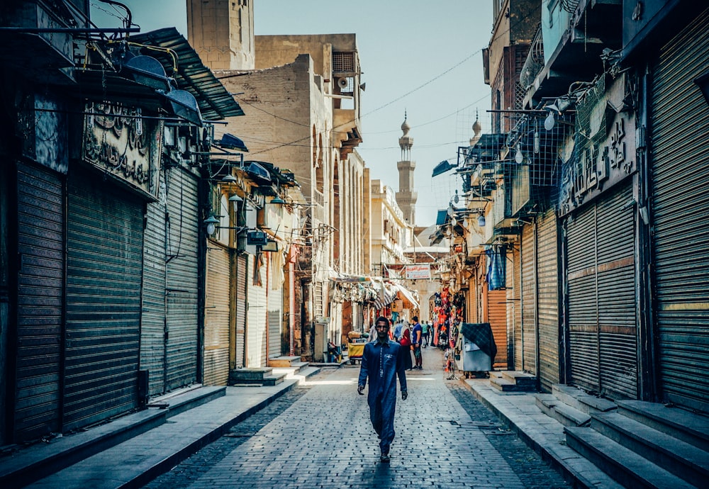 man walking on alley in between stores with closed roll-up doors at daytime