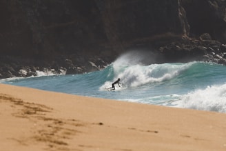 Aerial shot of a surfer catching a wave near a sunlit beach in the Lakes Region.