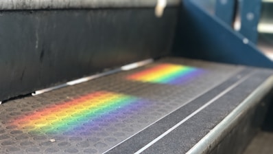 A close-up of a step featuring a textured, non-slip surface with a vibrant spectrum of rainbow colors reflecting across it. The rainbow effect is seen clearly on the dark surface, suggesting light induced refraction.