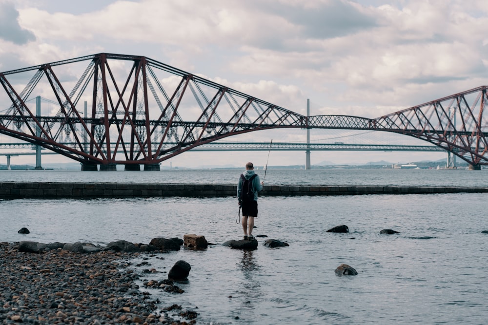 person in gray jacket standing on rock beside body of water