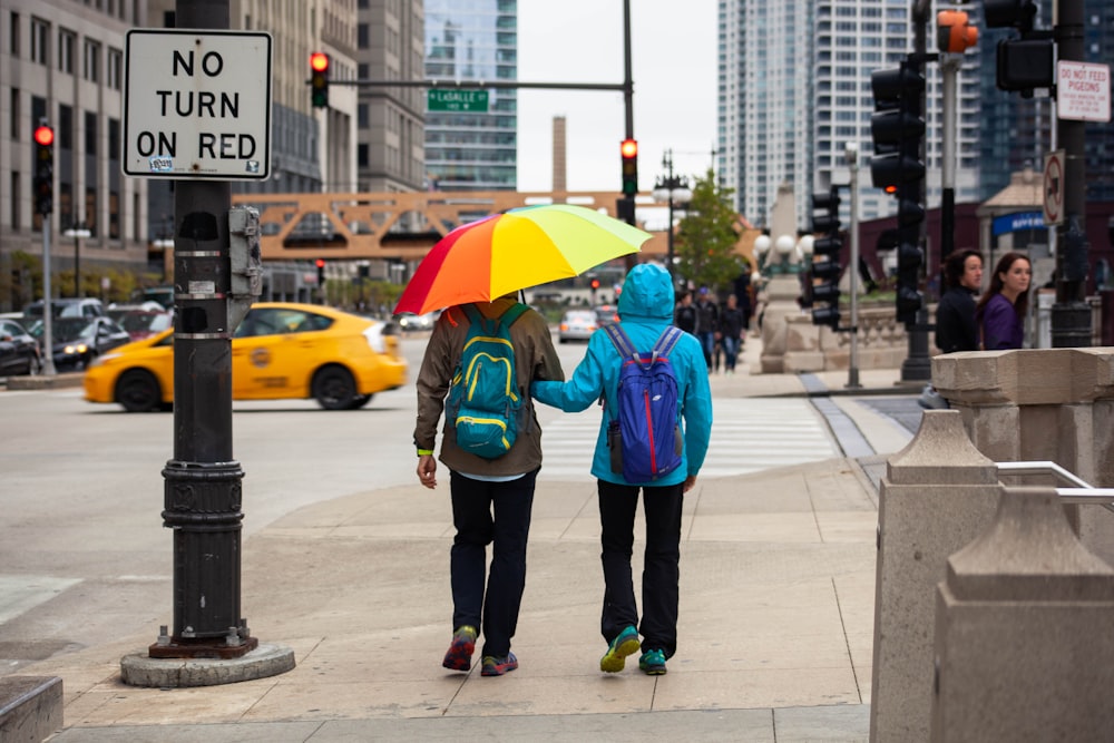 couple wearing jackets under colorful umbrella at the street
